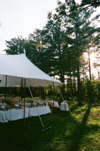 Wide landscape view of white sailcloth wedding tent at edge of pine forest in golden evening light