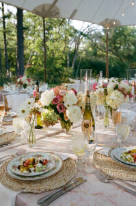 Colorful backyard wedding reception table set with food pink and white floral centerpieces and champagne glasses