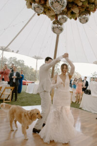 Bride and groom first dance under sailcloth tent groom spinning bride with golden retriever dog nearby