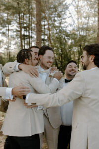 Groom and groomsmen in joyful group hug celebrating together in pine forest at backyard wedding