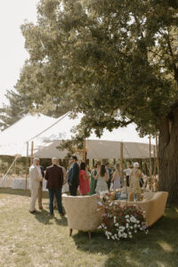 Guests mingling at outdoor backyard wedding reception under white sailcloth tent with large oak tree