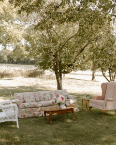 Vintage floral sofa and armchairs cocktail hour lounge under oak tree at backyard wedding