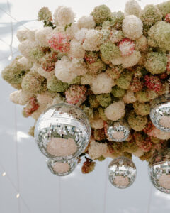 Close-up looking up at underside of wedding floral chandelier with cream blush and green hydrangeas and silver disco balls