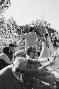 Black and white photo of bride and groom walking recessional with arms raised as guests set off confetti poppers
