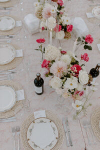 Wedding reception table detail with white and pink floral centerpiece wine bottle and gold rimmed plates