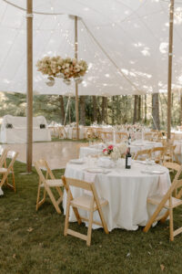 Backyard wedding tent interior before guests arrive with round tables wood chairs dance floor and floral chandelier installation