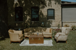 Vintage outdoor wedding lounge seating area with tufted sofa armchairs and leather trunk coffee table on lawn in front of brick house