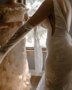 Close-up of bride getting ready as lace wedding dress is fastened showing intricate lace back detail